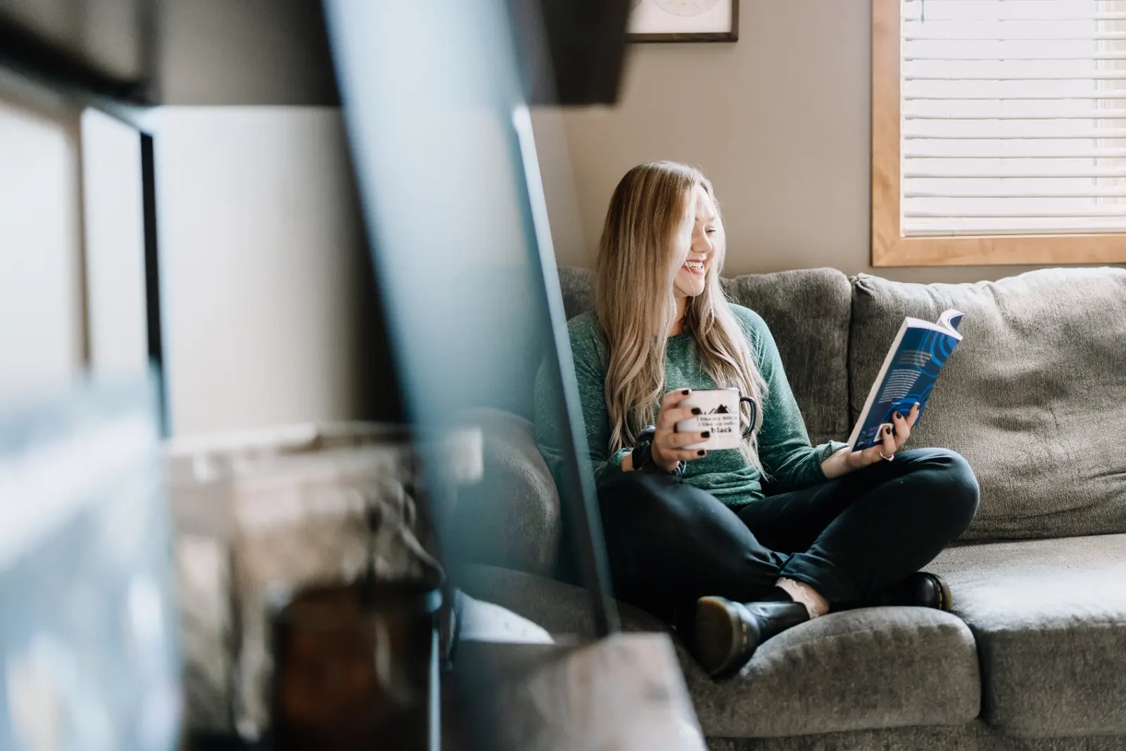 A woman curled up on a couch with coffee and a book — quiet reading time