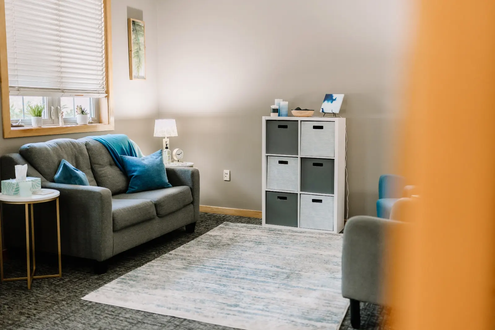 A calm, light-filled MK Counseling therapy room with a grey couch and blue accents