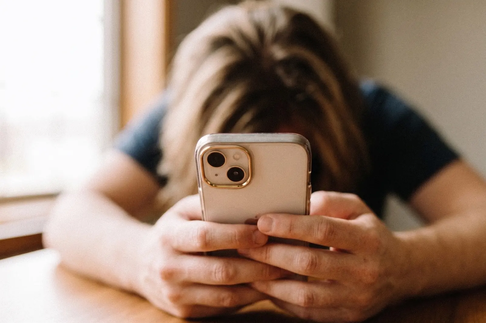 A person resting their head on their arms while holding a phone at a table